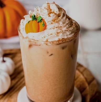 A glass of brown liquid with whipped cream and a small pumpkin decoration