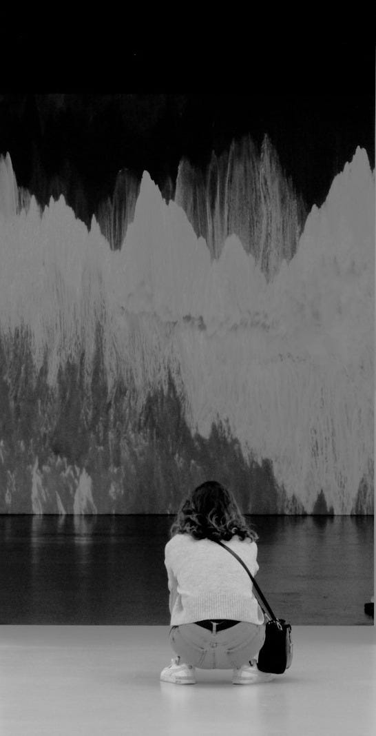 a black and white photo of a person sitting in front of a painting a black and white photo of a person sitting in front of a painting
