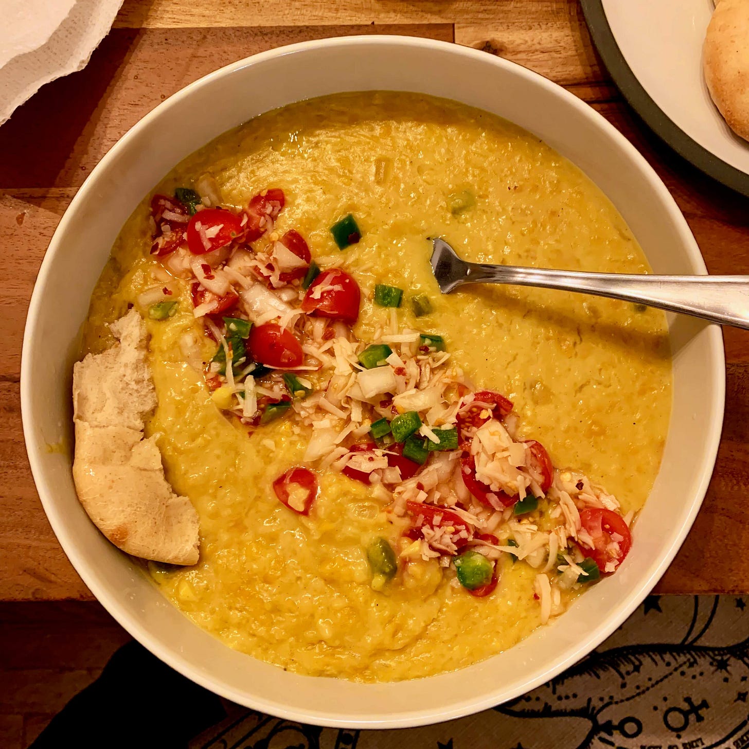 Bowl of yellow dal risotto with a streak of tomato-coconut sambol across the center and a piece of naan on the left.