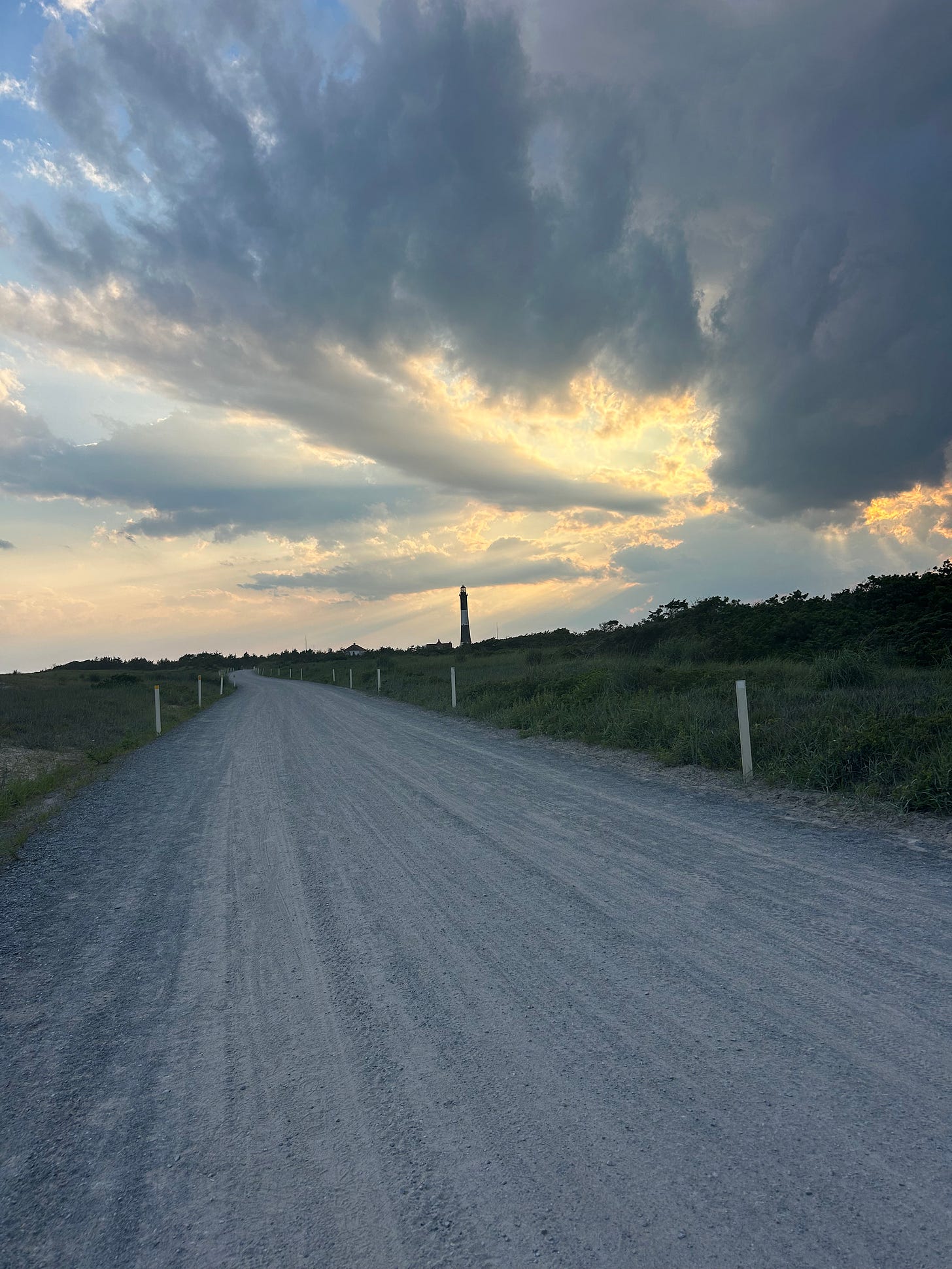 Sunset above a gravel path with a lighthouse in the background. Dune grass on either side