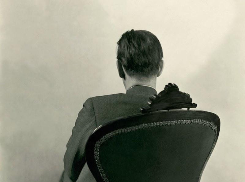Photograph of the back of a seated man.