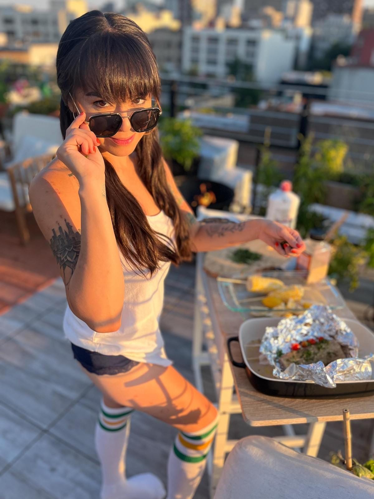 photo of a woman glancing over her sunglasses toward the camera while standing on a patio in brooklyn preparing veggies to be grilled