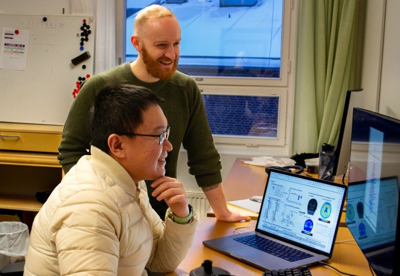 Lijun An is sitting at a desk in front of a laptop computer displaying...