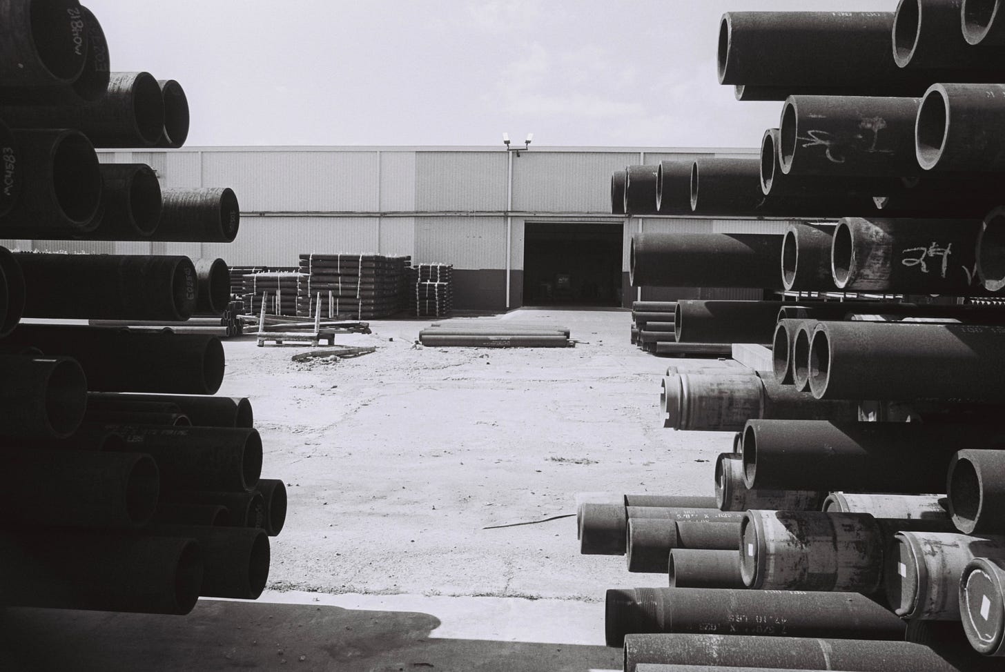 Black and white photo of pipeline segments stacked in an industrial yard Black and white photo of pipeline segments stacked in an industrial yard