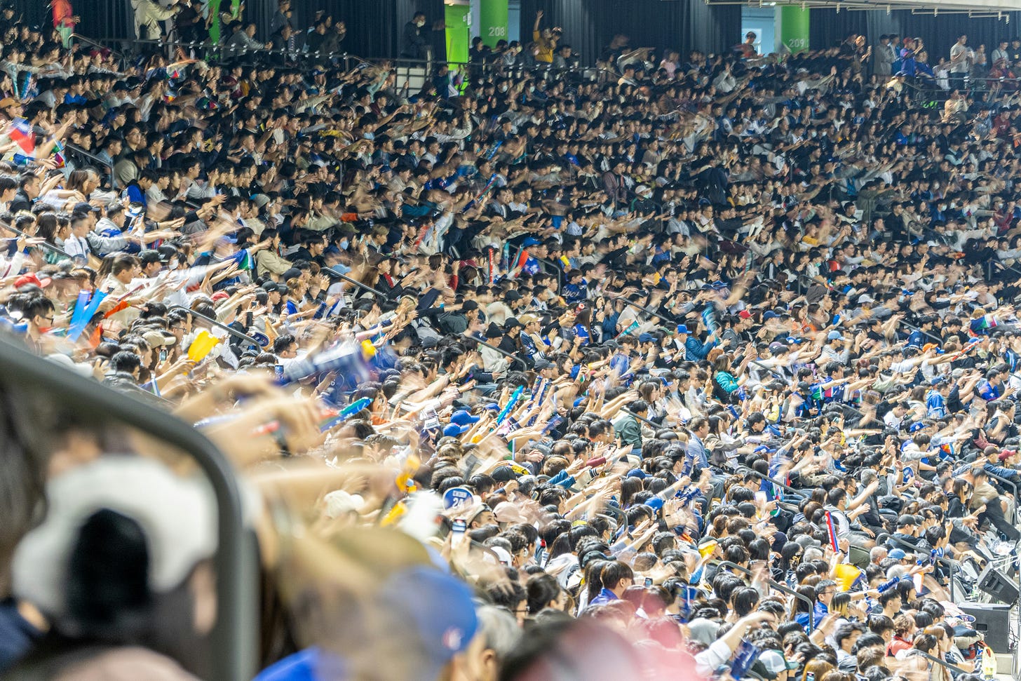 A wide-angle photograph taken from high in the stands of a crowded baseball stadium during the World Baseball Classic. A massive crowd of fans is seen waving their arms and hands in a coordinated, celebratory motion, many holding small flags or cheering noisily. The photo is full of kinetic energy and demonstrates a massive, unified cheer. The perspective is from the left field stands, looking towards the right.