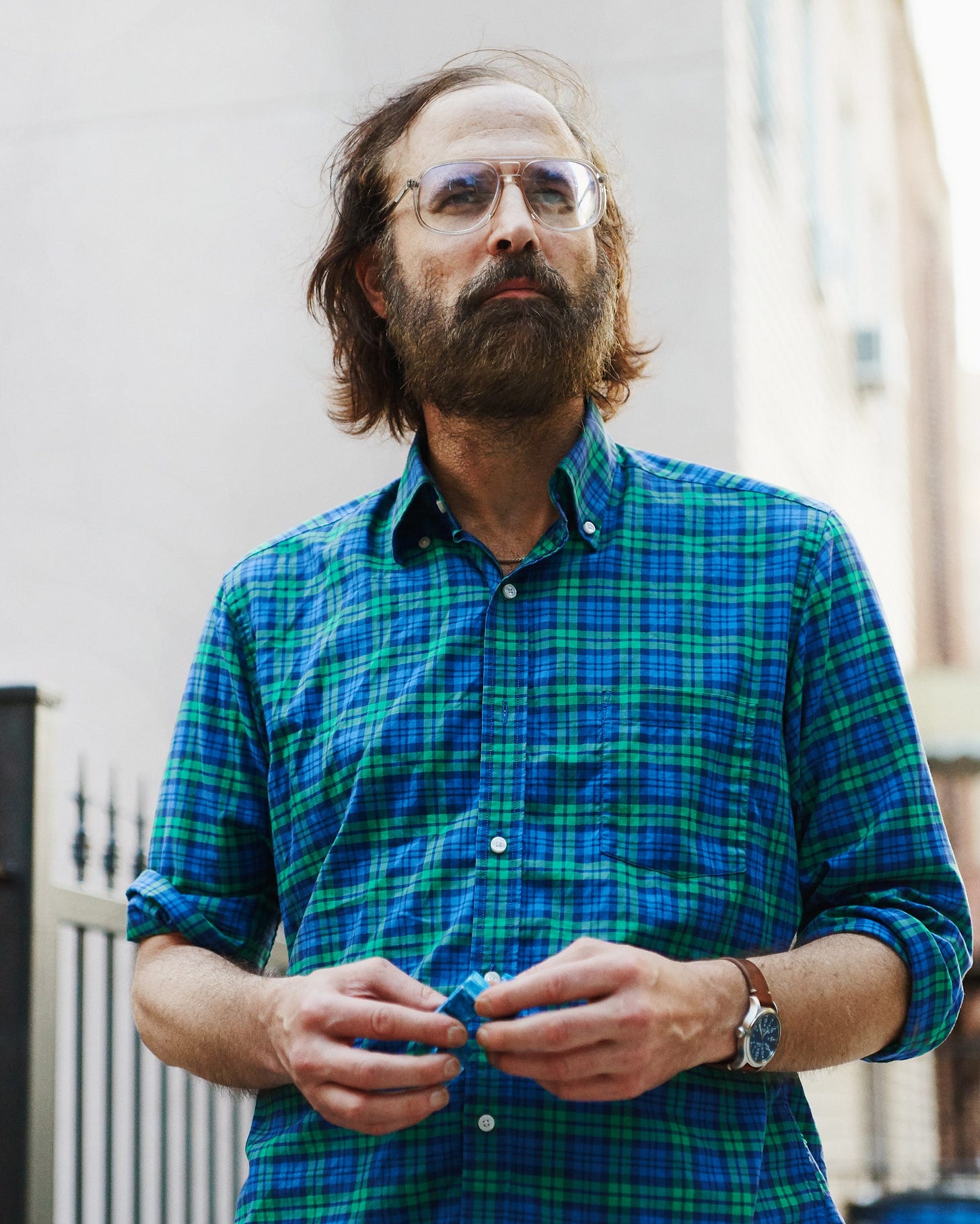 David Berman standing looking off in to the distance in a blue and green plaid shirt.