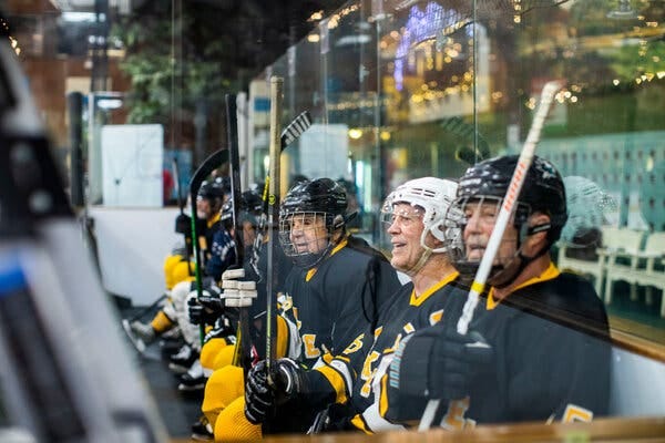 Players in black uniforms with yellow letters diagonally across the front sit on a bench.