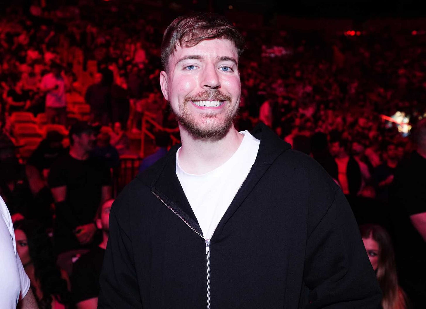A photograph of Jimmy Donaldson, aka MrBeast, smiling at the camera. A huge crowd of people is behind him