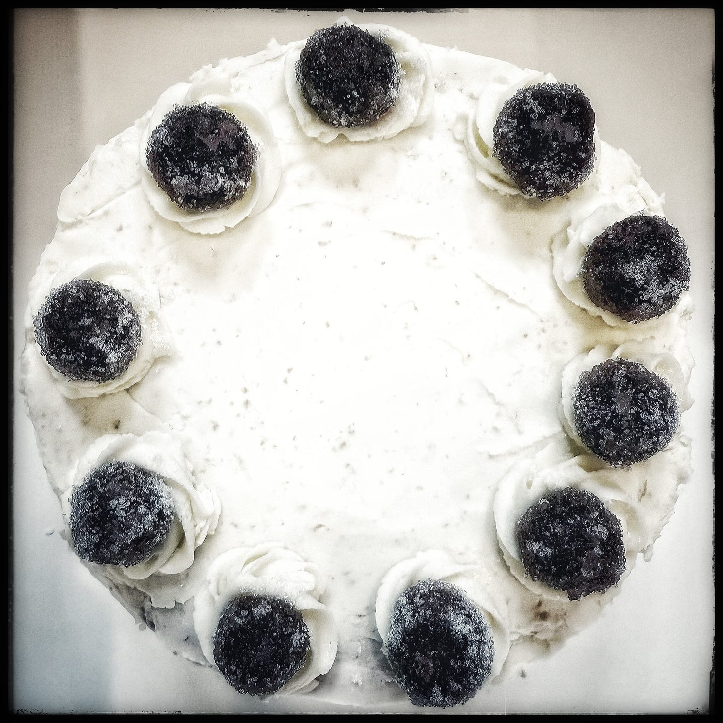 Overhead view of a small cake covered in vanilla buttercream frosting and topped with Amarena cherries. 