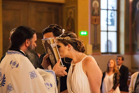 An American bride kisses a bible in a Greek Orthodox wedding ceremony, immediately regrets getting lipstick on it. The happy couple afterward at the beautiful candle-lit reception