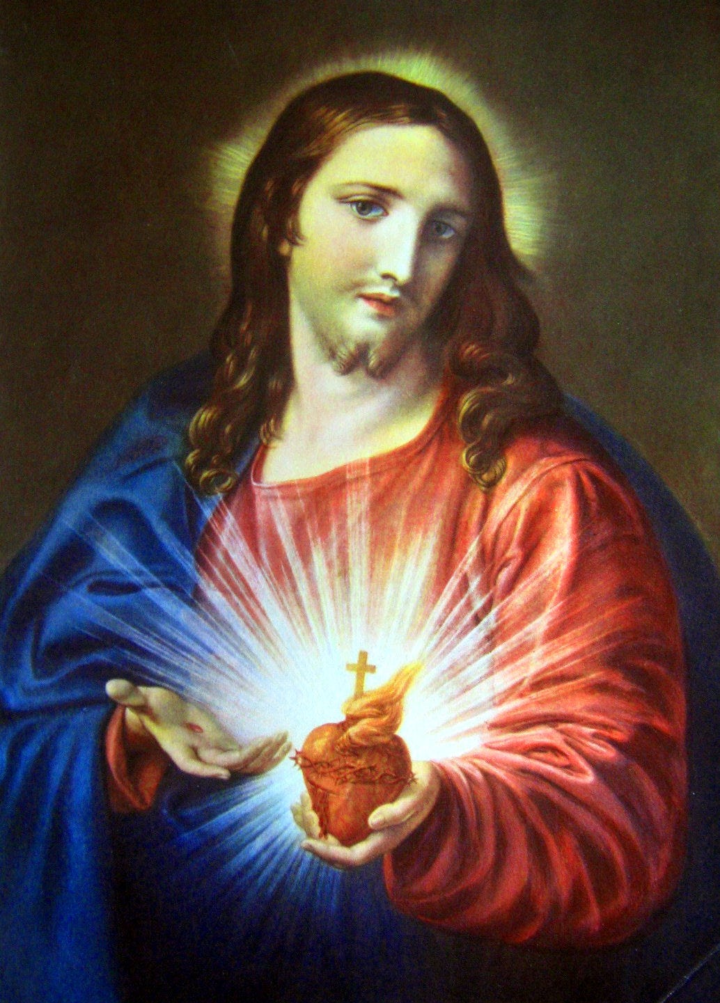 painting of the Sacred Heart of Jesus. White Jesus with long brown hair wears a red and blue robe. He holds a glowing heart decorated with a gold cross.