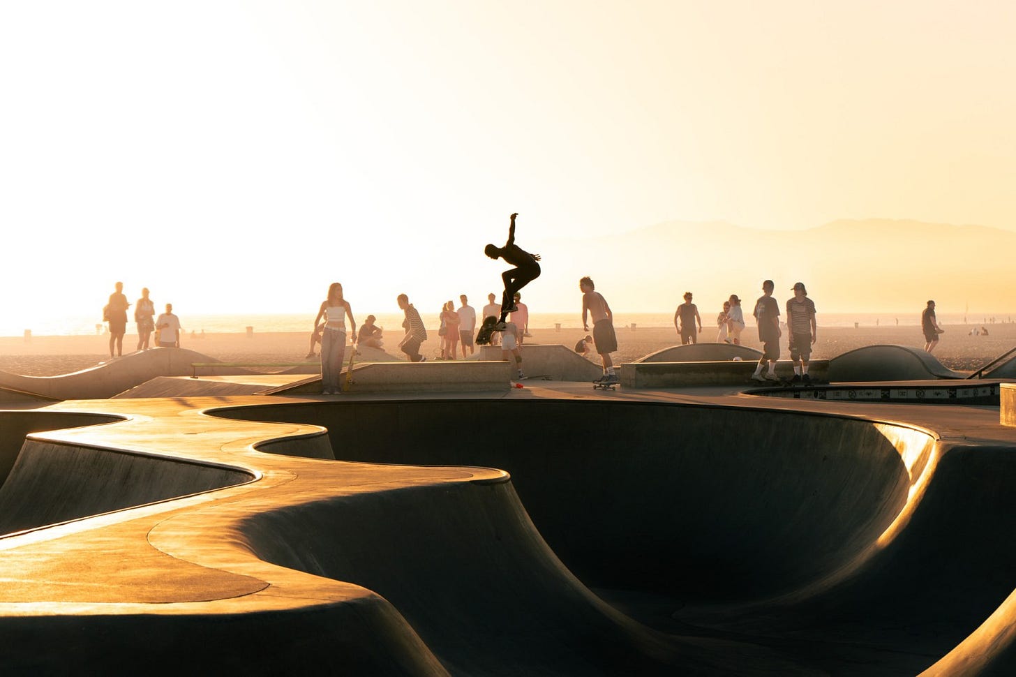 Silhouette of a skateboarder mid-air at sunset in a skatepark.