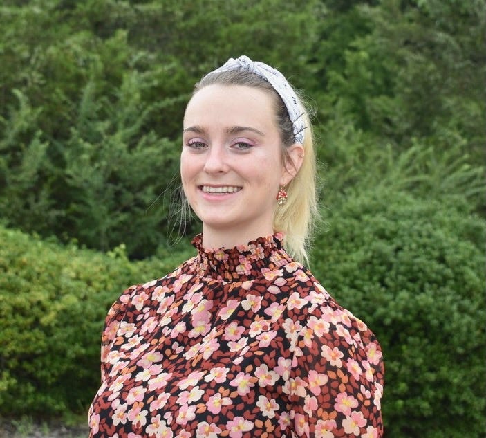 A student with a floral shirt against a background of greenery