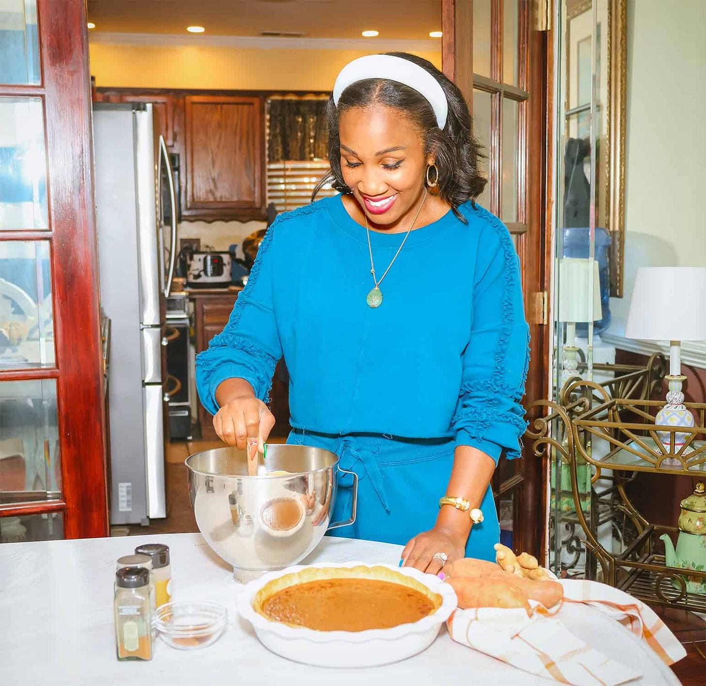 Soul food cookbook author, Shaunda Necole of The Soul Food Pot, mixing homemade Southern sweet potato pie filling in a stainless-steel bowl, with a pie shell, fresh sweet potatoes, and warm holiday spices displayed on the counter — classic soul food Thanksgiving dessert preparation.