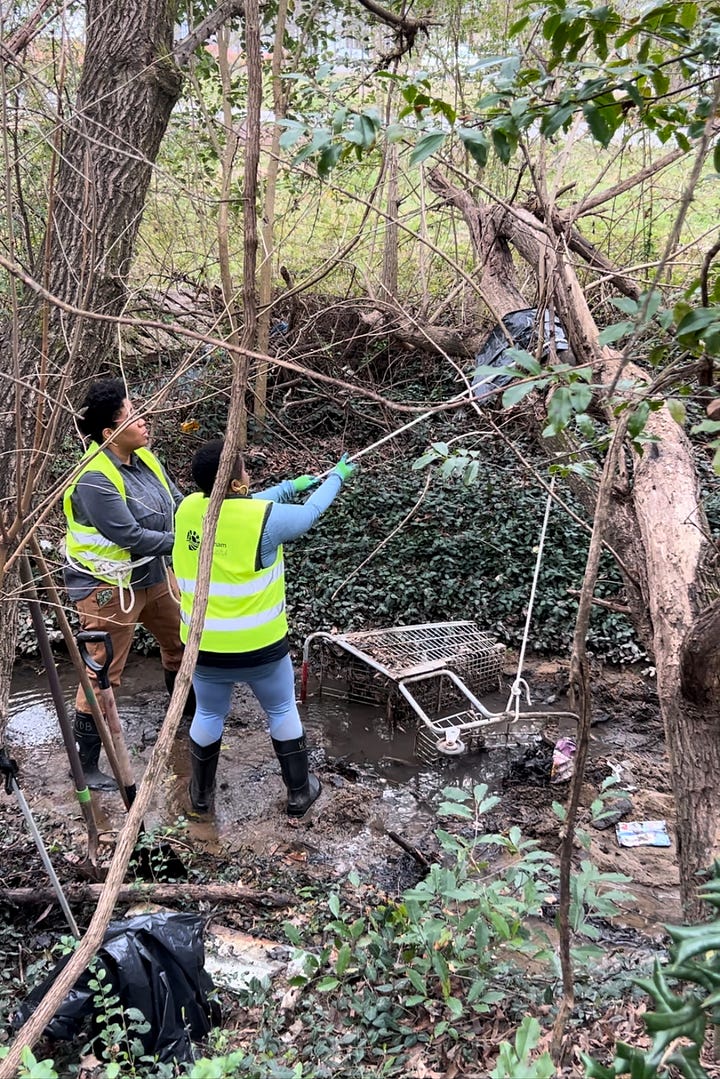 first picture: two black people in neon yellow vests in a creek pulling on a white rope pulley connected to a shopping cart. Second photo is a young man in a black hat and neon nest pulling on the rope