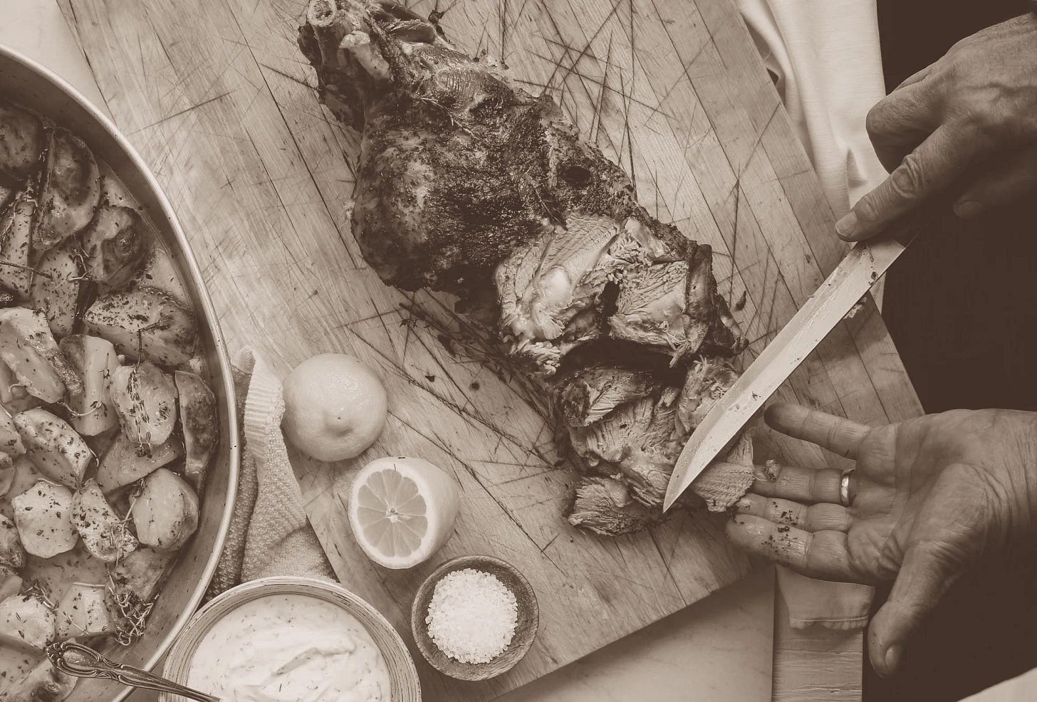 a Birds Eye view of a leg of lamb being carved with a dish of roast potatoes to the side