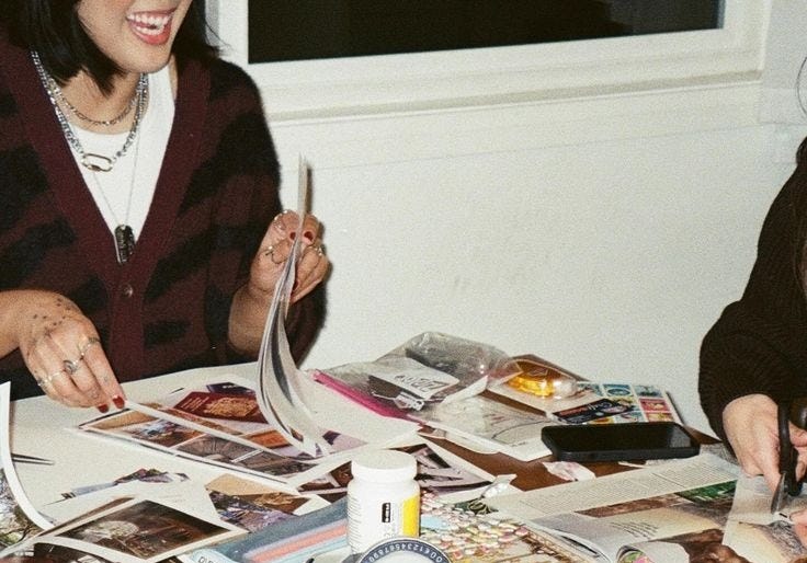 This may contain: two women are sitting at a table covered with magazines and photos, one is holding a cell phone This may contain: two women are sitting at a table covered with magazines and photos, one is holding a cell phone