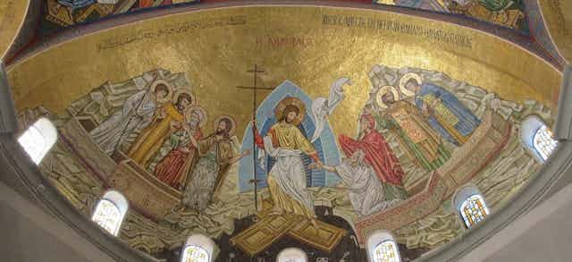 A mosaic with a golden background, six figures with halos, Jesus holding a cross in the middle, and two people whom he is helping out of coffins. A mosaic with a golden background, six figures with halos, Jesus holding a cross in the middle, and two people whom he is helping out of coffins.