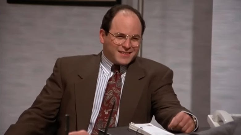 George Costanza in a brown suit, sitting opposite his boss' desk. George Costanza in a brown suit, sitting opposite his boss' desk.