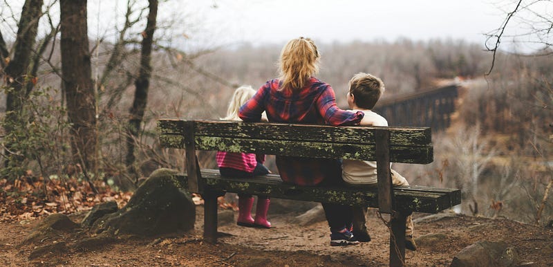A woman sits with two kids on a bench.