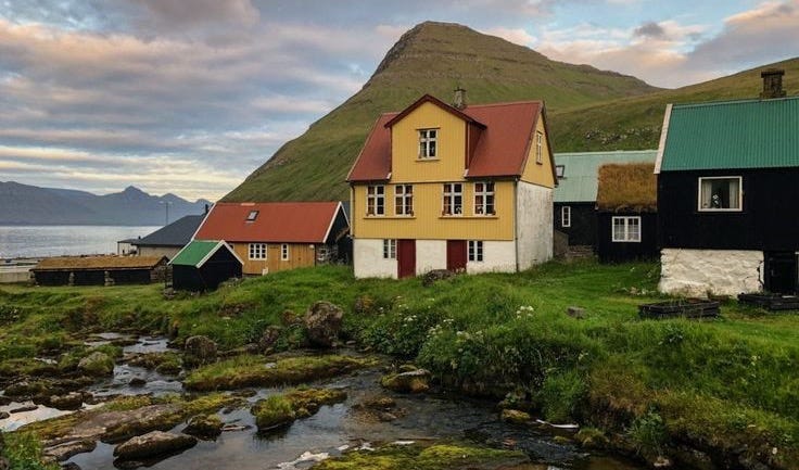 This may contain: some houses are sitting on the side of a hill near a small stream and water