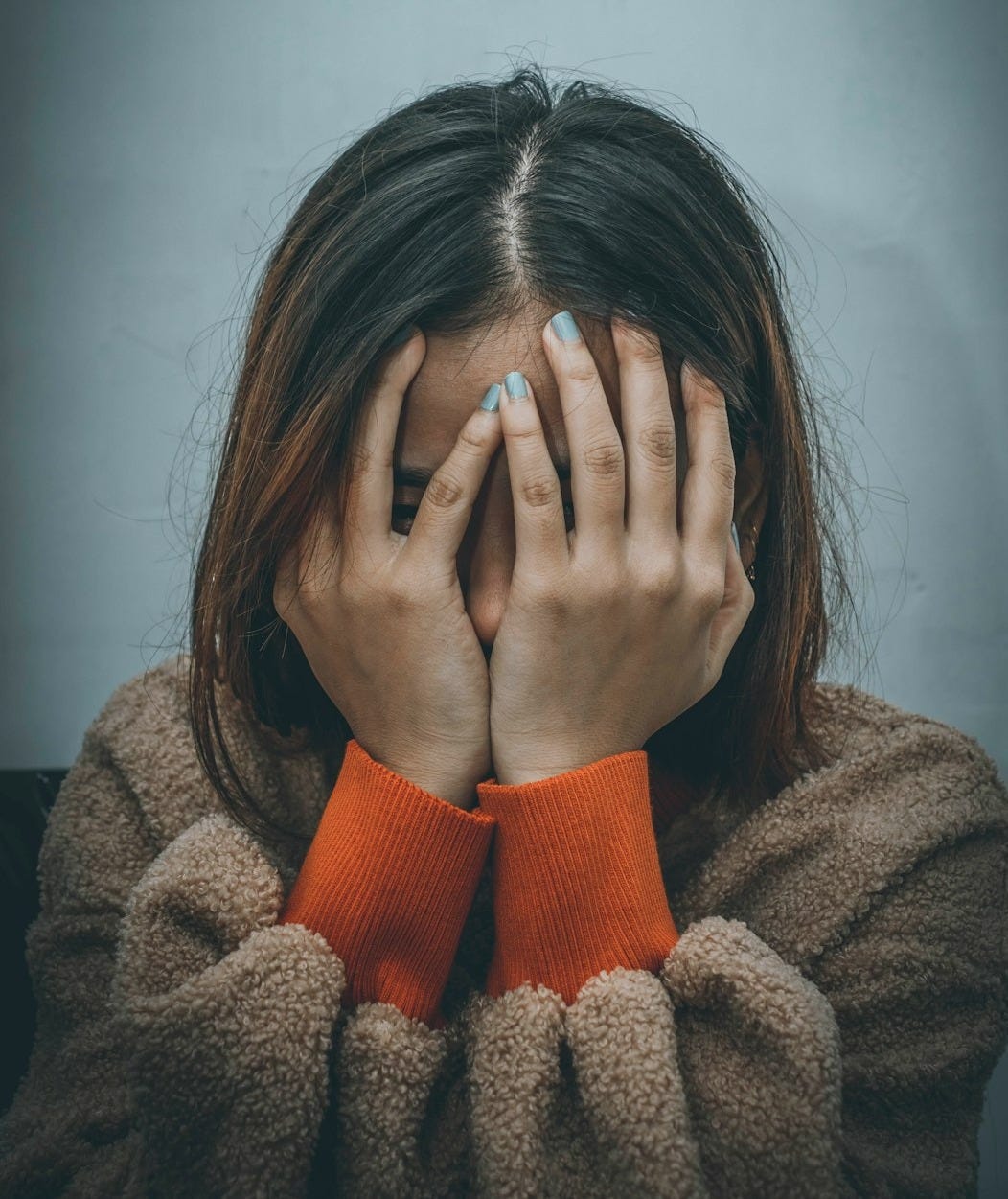 woman in brown sweater covering her face with her hand