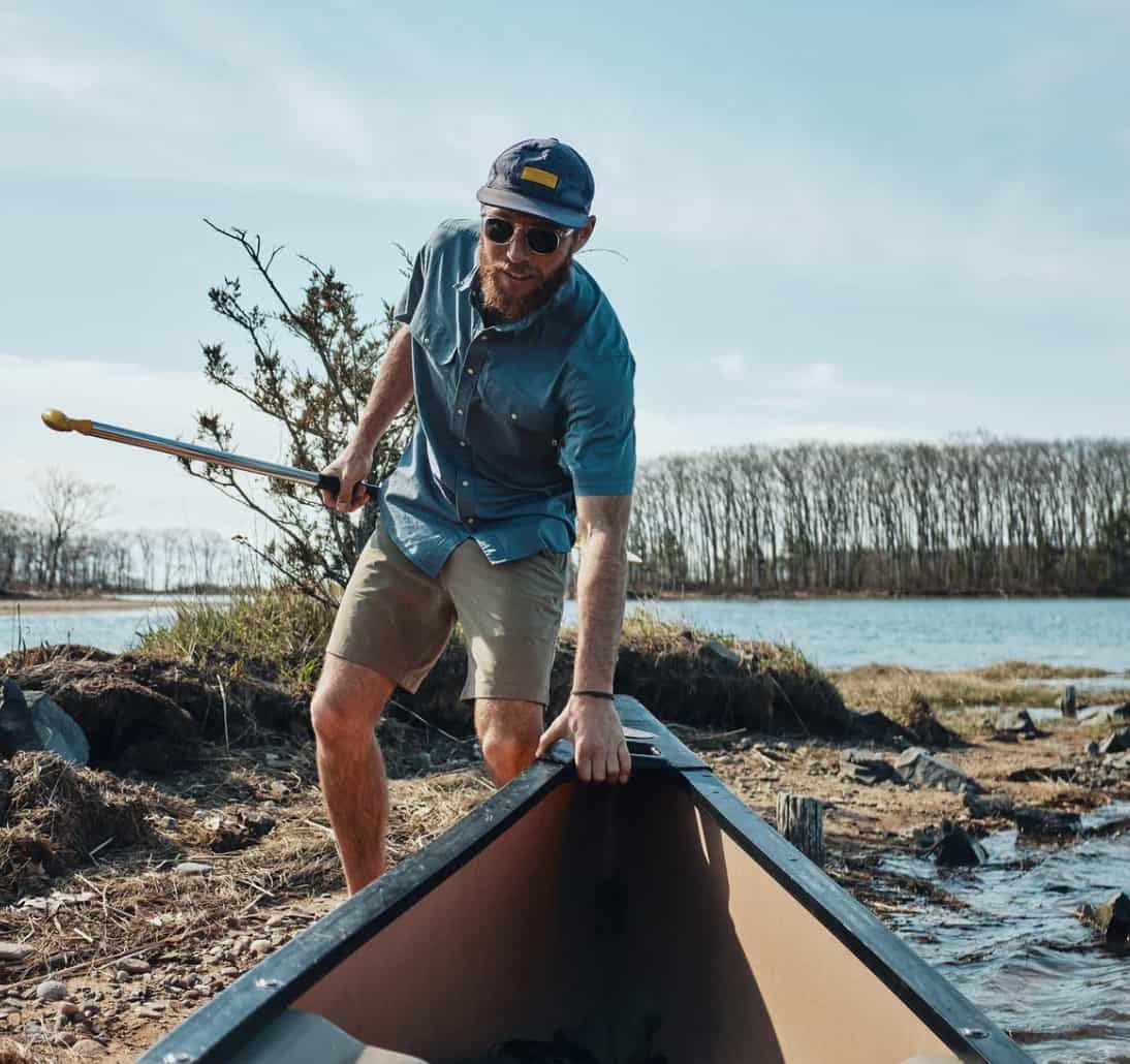 man wearing wellen eddy shirt pushes a canoe into a lake