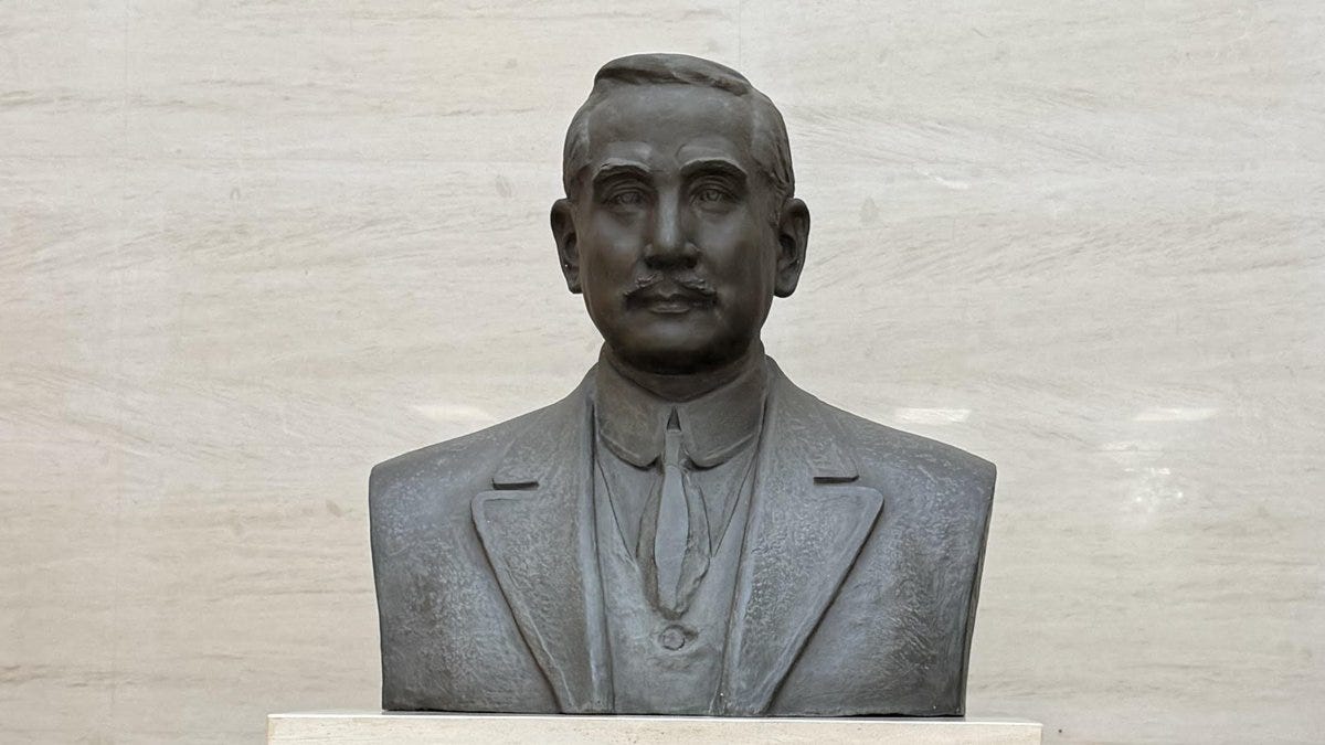 A bronze bust of Sun Yat-sen, depicting him in a suit and tie, positioned against a marble background.