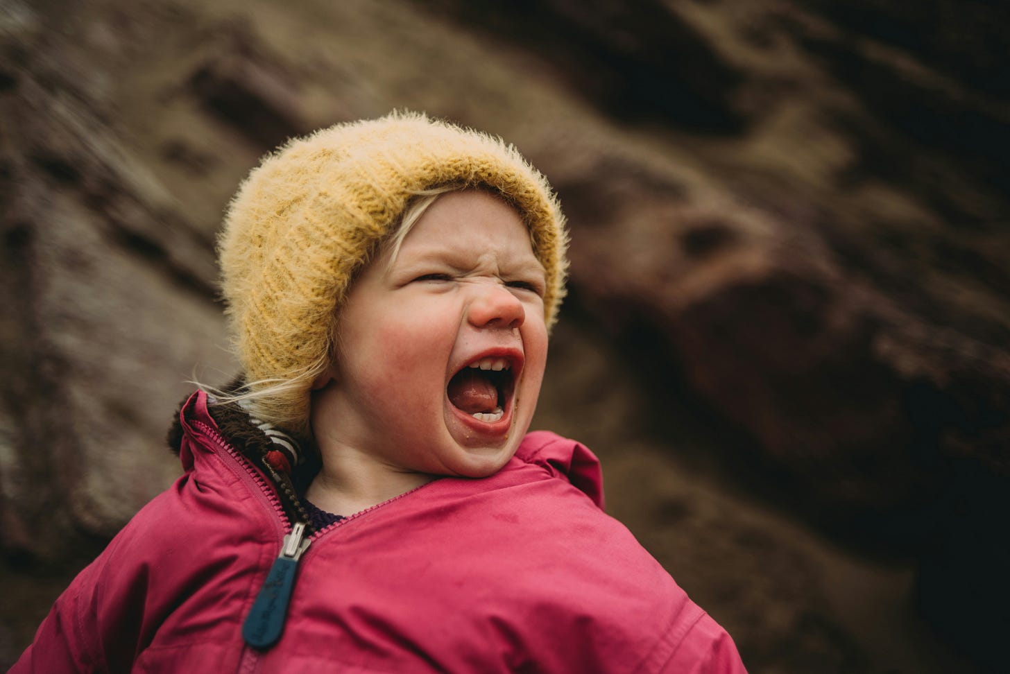 A white child in winter clothing turned at an awkward angle, grimacing and yelling. 