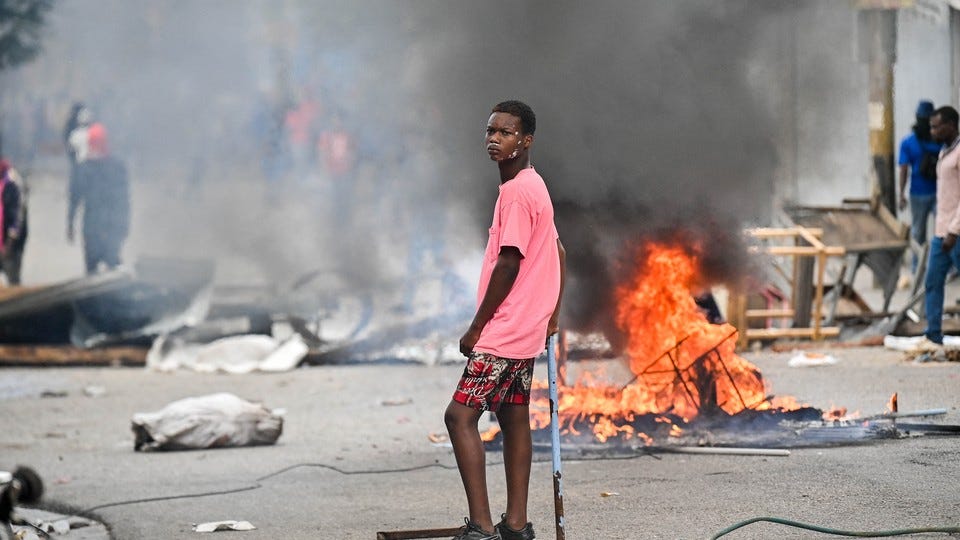A young man stands in a city street where a fire is burning, emitting a cloud of black smoke. A young man stands in a city street where a fire is burning, emitting a cloud of black smoke.