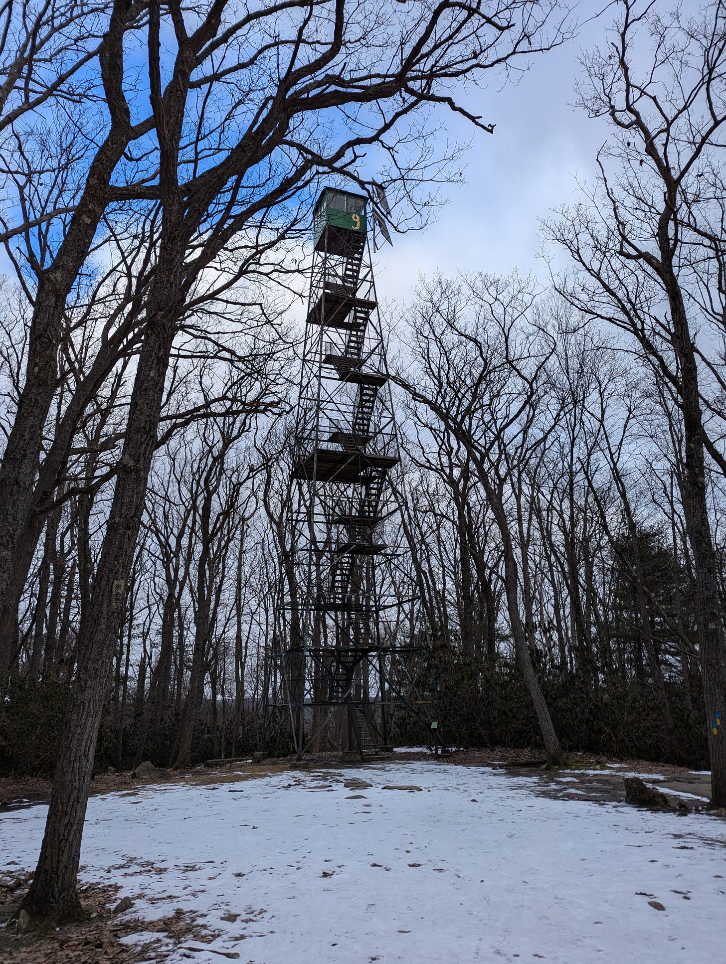 Old Fire Tower #9 stands against a blue sky. A box at the top of the tower has a yellow "9" painted on it.