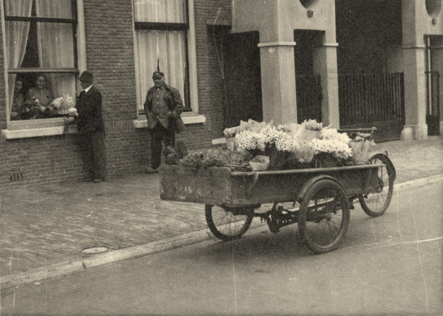 An old black and white photo showing a cargobike covered in flowers which are being sold. An old black and white photo showing a cargobike covered in flowers which are being sold.