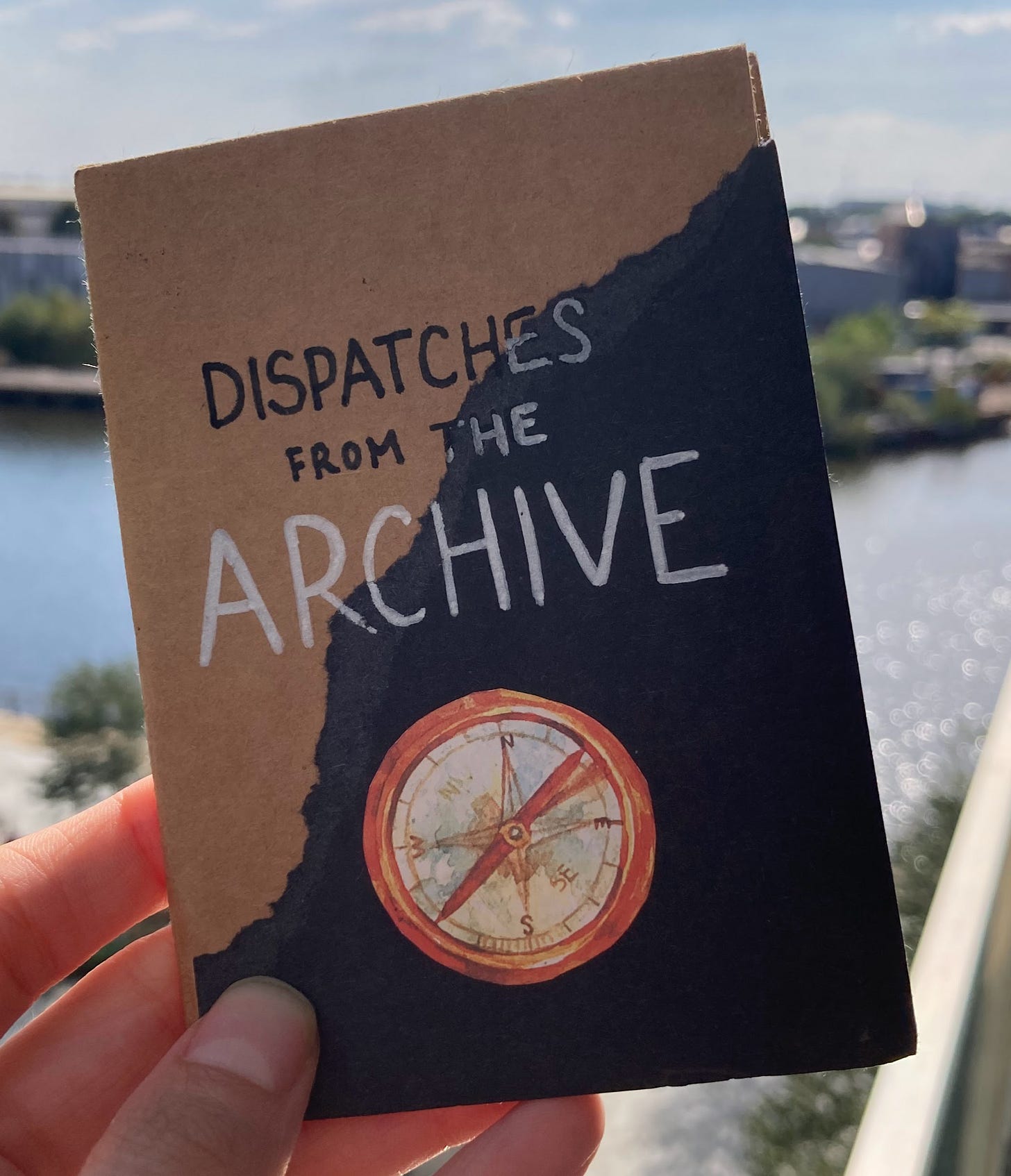 Dispatches from the Archive, title page with compass sticker against a brown background with torn black paper cutting diagonally across the cover