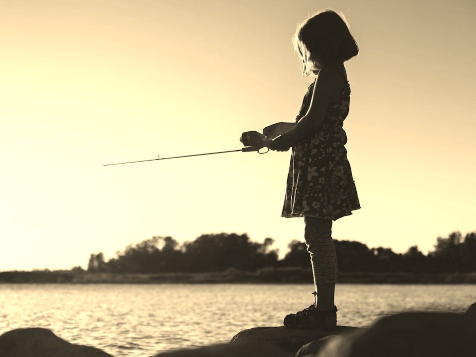 woman in white and black dress holding fishing rod standing on rock near body of water