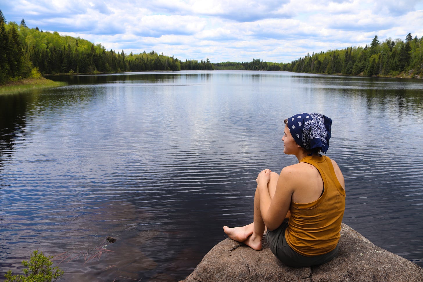 Picture shows Lisa sitting on a serene lake, sitting without a pack, obviously relishing in the lightness of the moment.