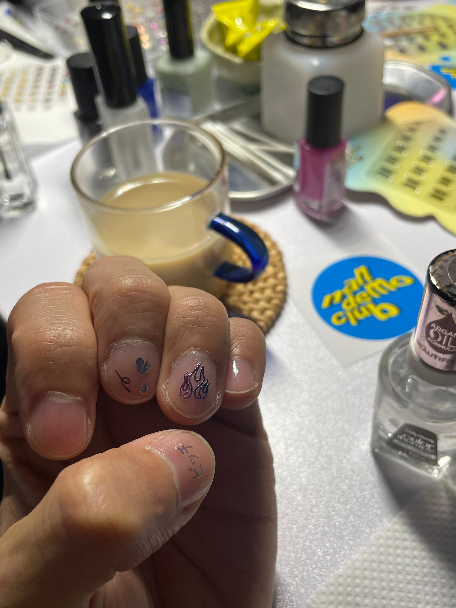 ネイル会の様子。テーブルの上にネイルの道具やネイルシールがたくさん置かれている。手前に著者の左手が写っていて、親指にシルバーの文字で「ビッチ」と書かれたネイルシールが貼られている。