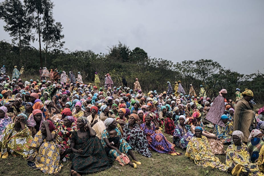 A group of women seated outdoors, many wearing cloth wraps and headscarves A group of women seated outdoors, many wearing cloth wraps and headscarves