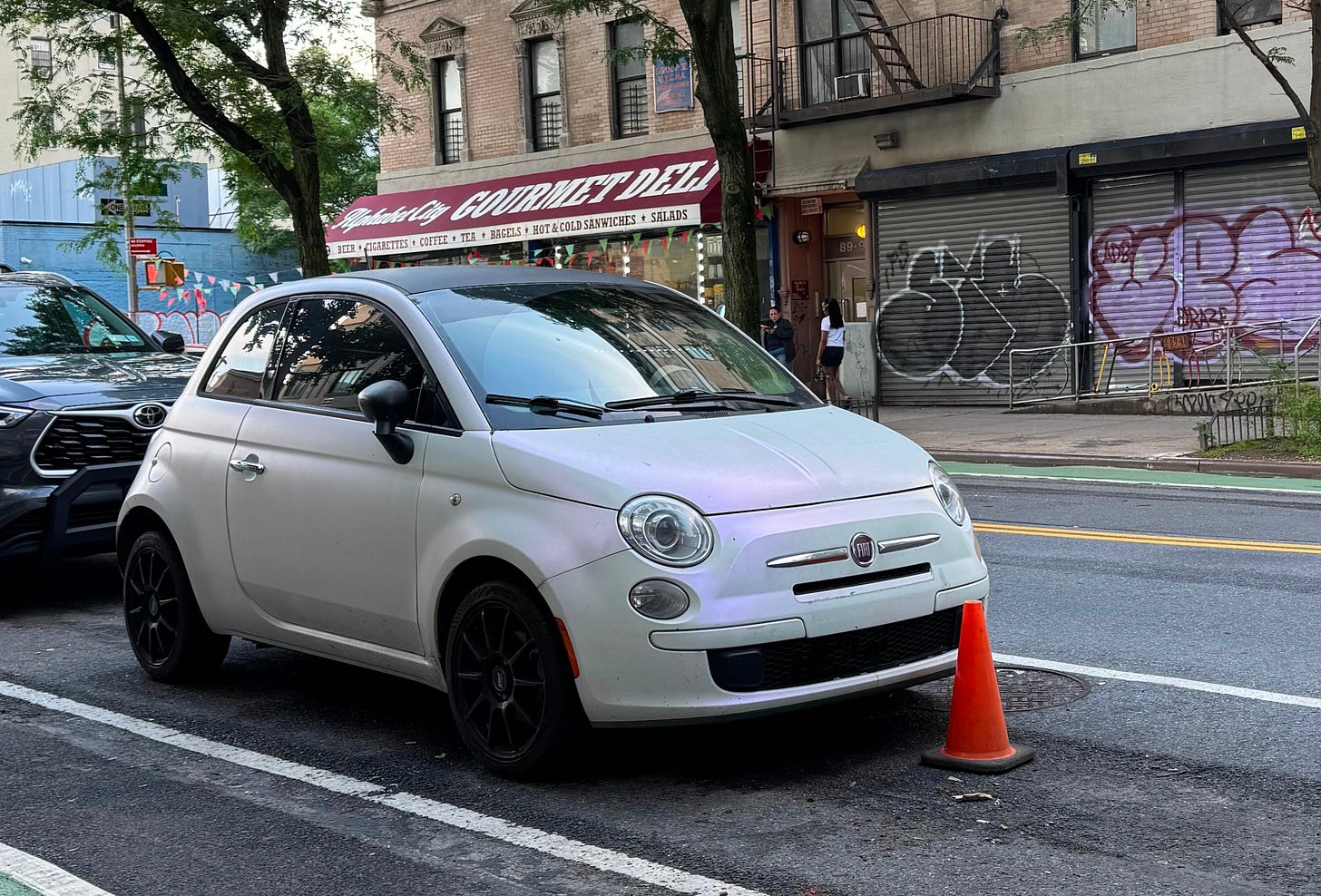 parked white Fiat with a small orange cone in front of it on nyc street