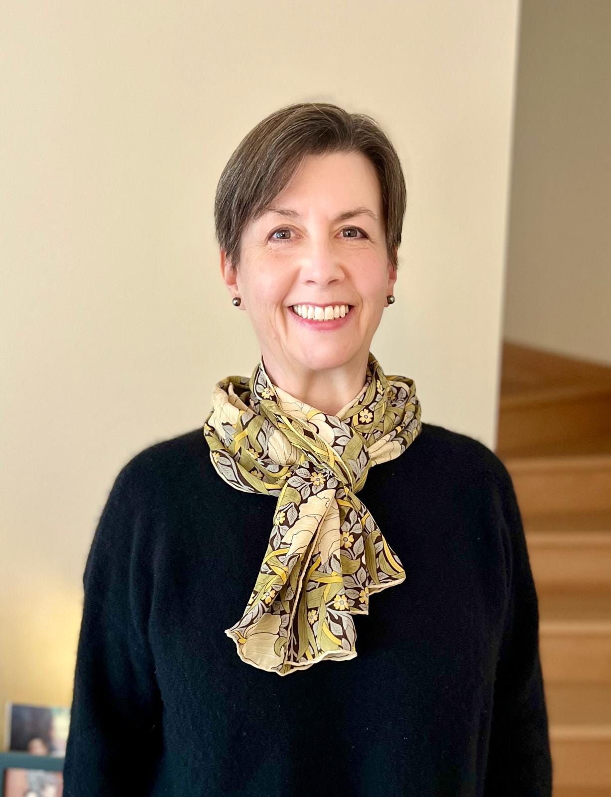 A woman with short hair smiles at the camera. She is wearing a flowered scarf and a black sweater.
