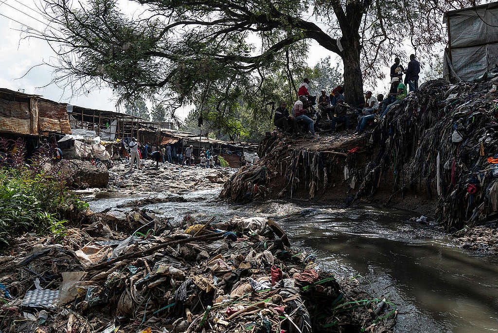 Fast Fashion Research in Kenya. © Kevin McElvaney / Greenpeace Image of the clooged-up Nairobi River through the Gikomba market in Kenya. The photo shows the banks of the water stream covered in waste. Very little parts of the ground can be seen through the amount of waste.