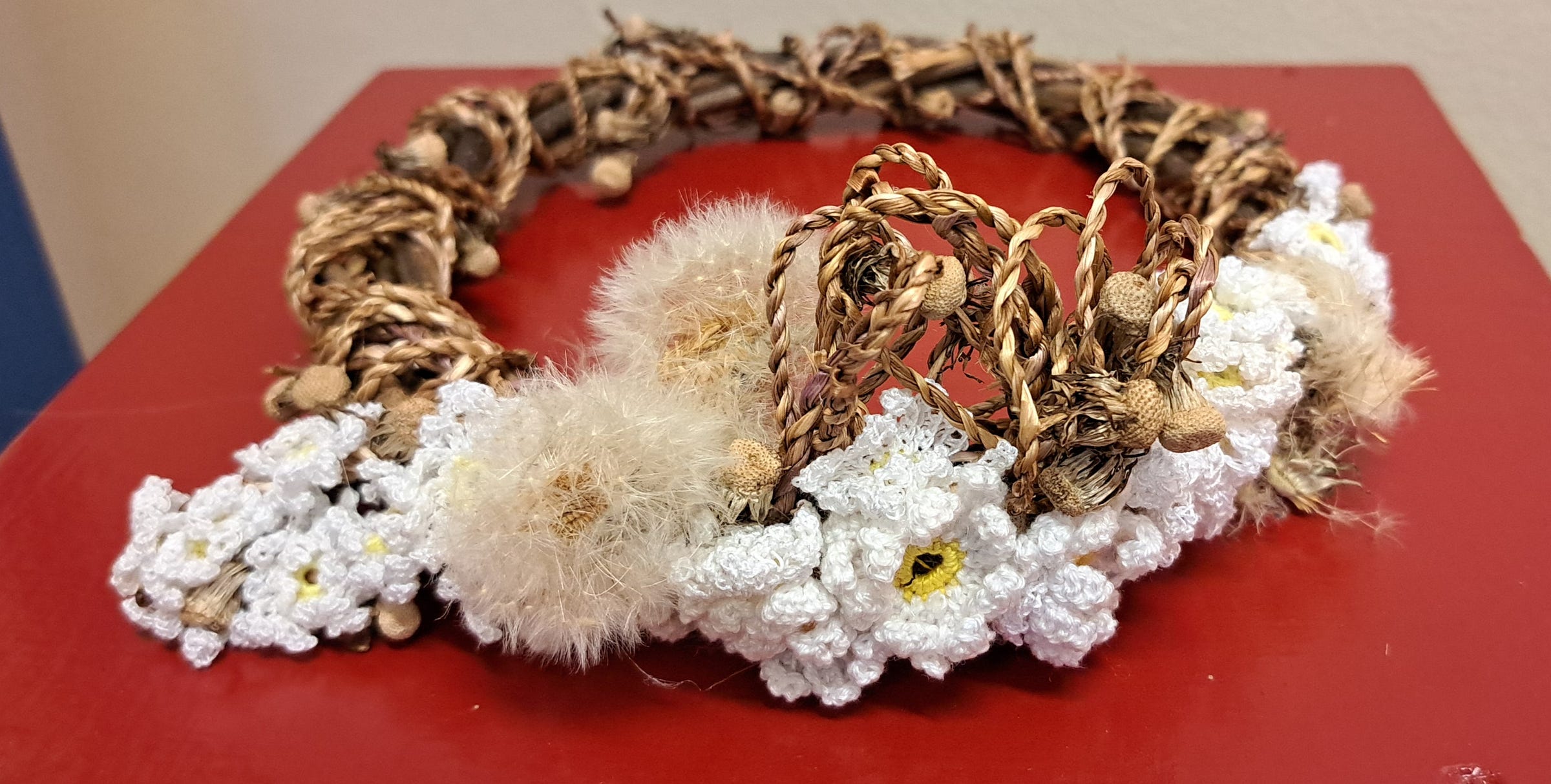 A circlet or crown woven from willow branches and wound with chunky golden dandelion cordage. At the front are some lace flowers with pale yellow centres, and some dandelion 'clocks' - fluffy seedheads. A circlet or crown woven from willow branches and wound with chunky golden dandelion cordage. At the front are some lace flowers with pale yellow centres, and some dandelion 'clocks' - fluffy seedheads.