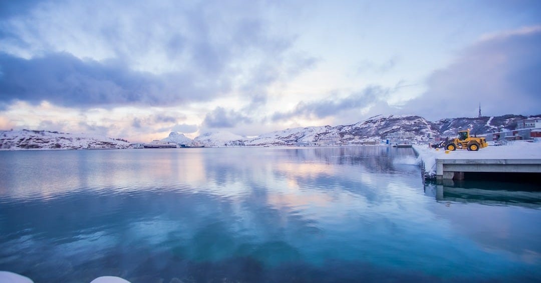 white and black house on snow covered ground near body of water under white clouds and white and black house on snow covered ground near body of water under white clouds and