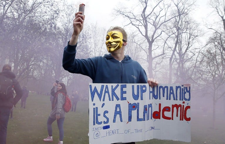 A protester with a flare poses holding a sign calling for people to "wake up" during a "World Wide Rally For Freedom" protest in London, England. A protester with a flare poses holding a sign calling for people to "wake up" during a "World Wide Rally For Freedom" protest in London, England.