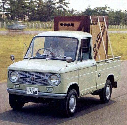 This may contain: an old pick up truck driving down the road in front of some grass and trees