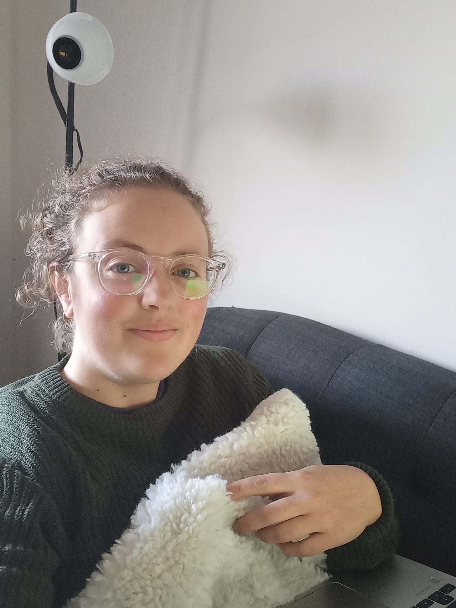 Alyssa in a cozy sweater on the couch with her laptop, smiling awkwardly at the camera.