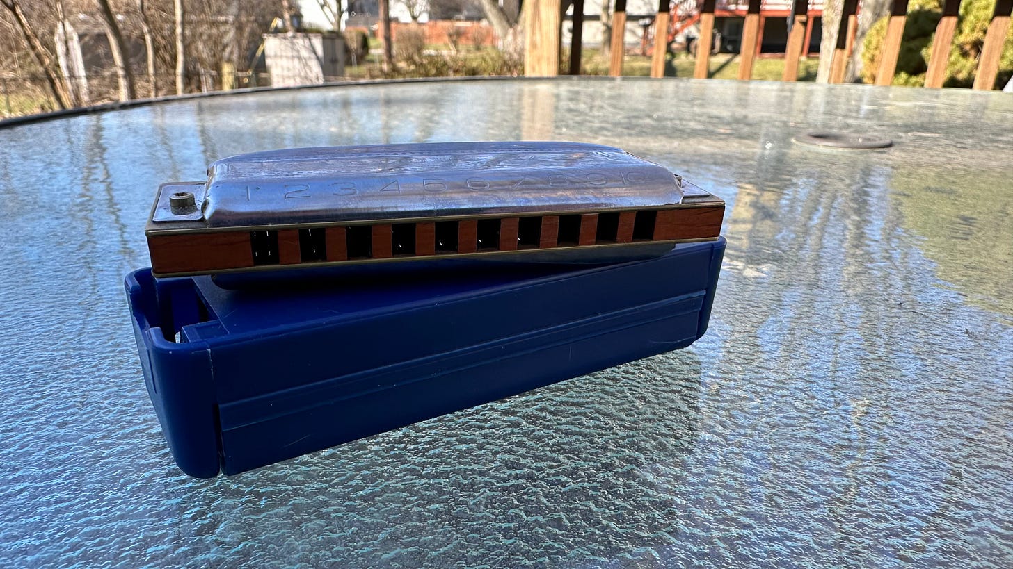 A harmonica perched on top of its case sitting on a back deck table A harmonica perched on top of its case sitting on a back deck table