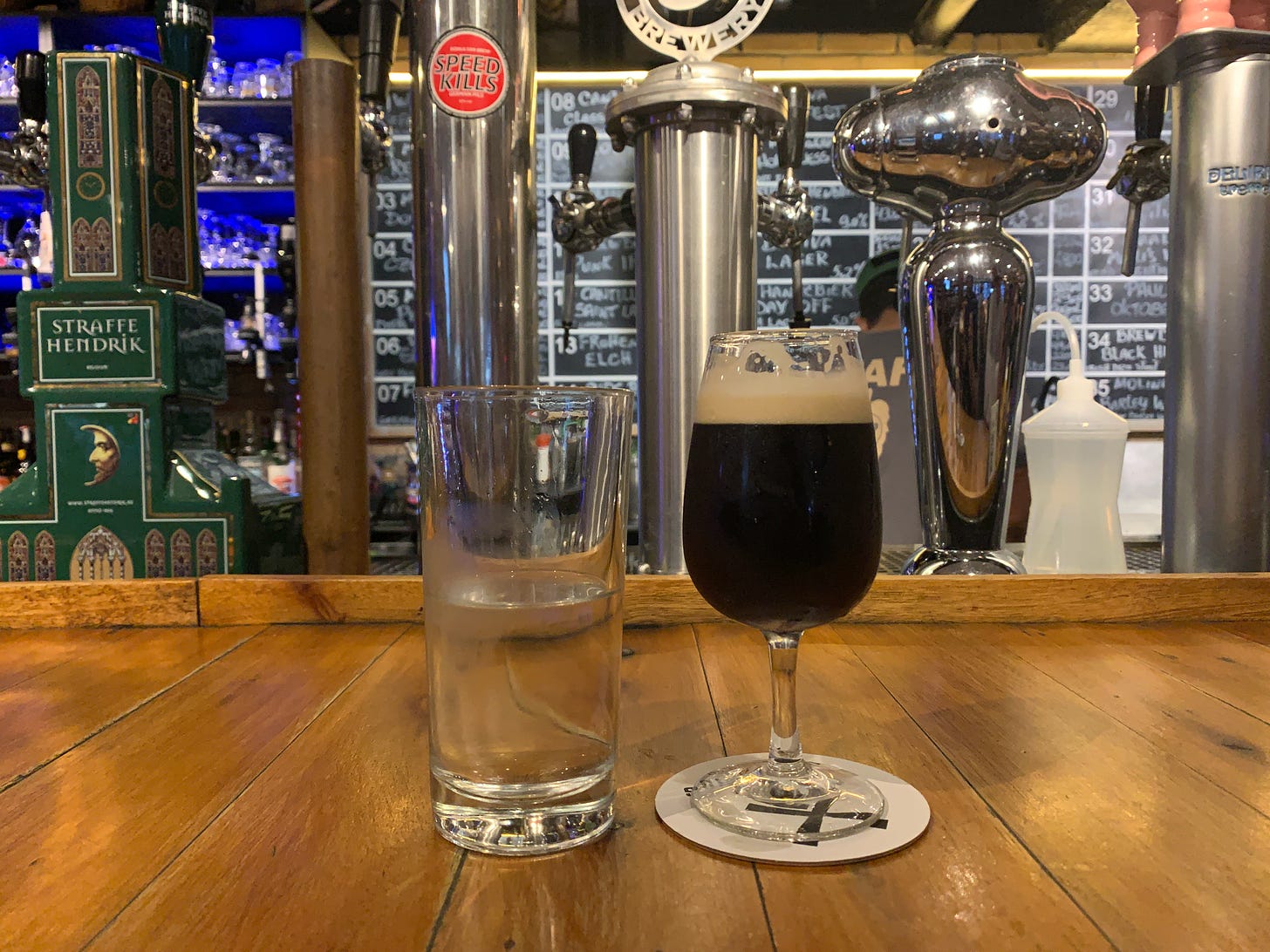 Dois copos num balcão de bar de cervejaria; um tem água, o outro contém cerveja escura. 