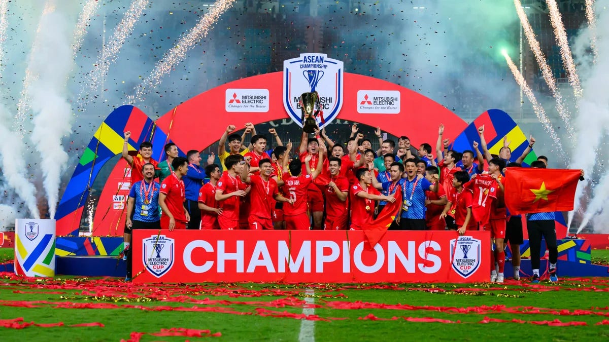 The Vietnam national football team celebrates winning the 2024 AFF Mitsubishi Electric Cup with the trophy on stage, surrounded by fireworks and confetti. The Vietnam national football team celebrates winning the 2024 AFF Mitsubishi Electric Cup with the trophy on stage, surrounded by fireworks and confetti.