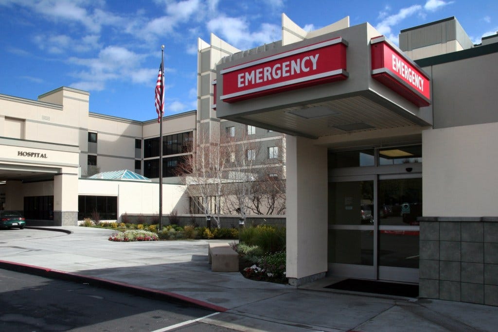 The outside of a rural hospital, image focused on the emergency room entrance. The outside of a rural hospital, image focused on the emergency room entrance.