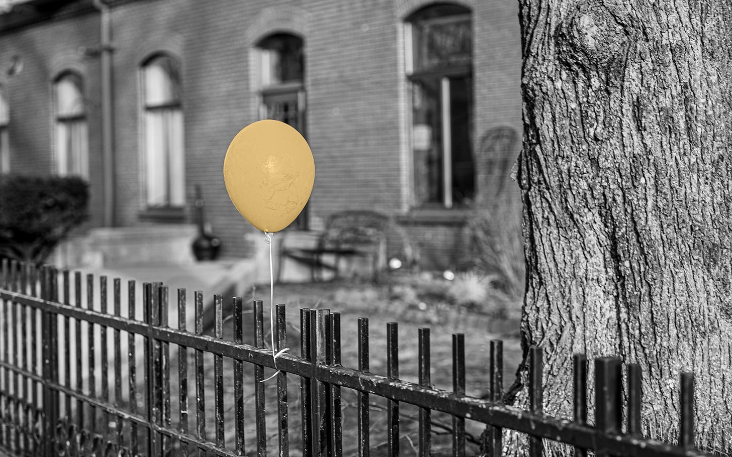 Single yellow balloon flys above a fence in front of an apartment building Single yellow balloon flys above a fence in front of an apartment building